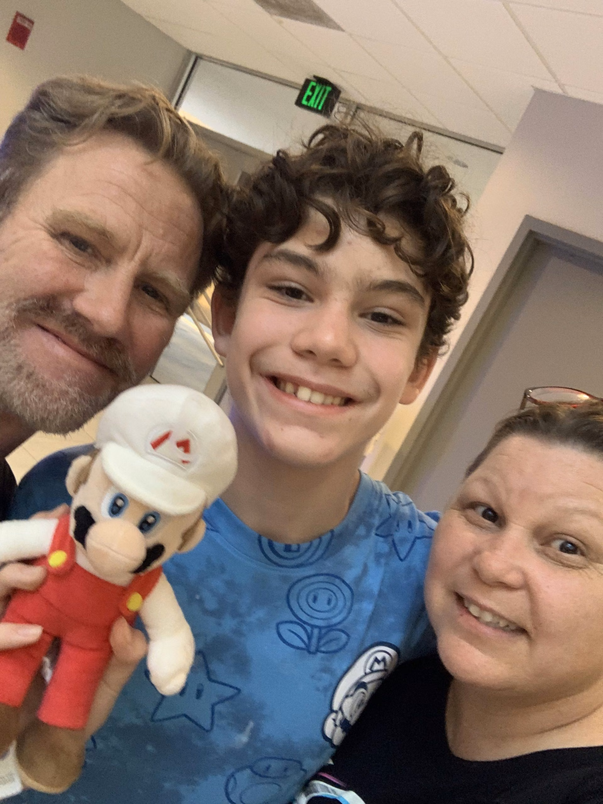 A family selfie — mom, dad, and their son holding a Mario plush